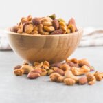 A bowl of flavored nuts standing on a grey background surface.