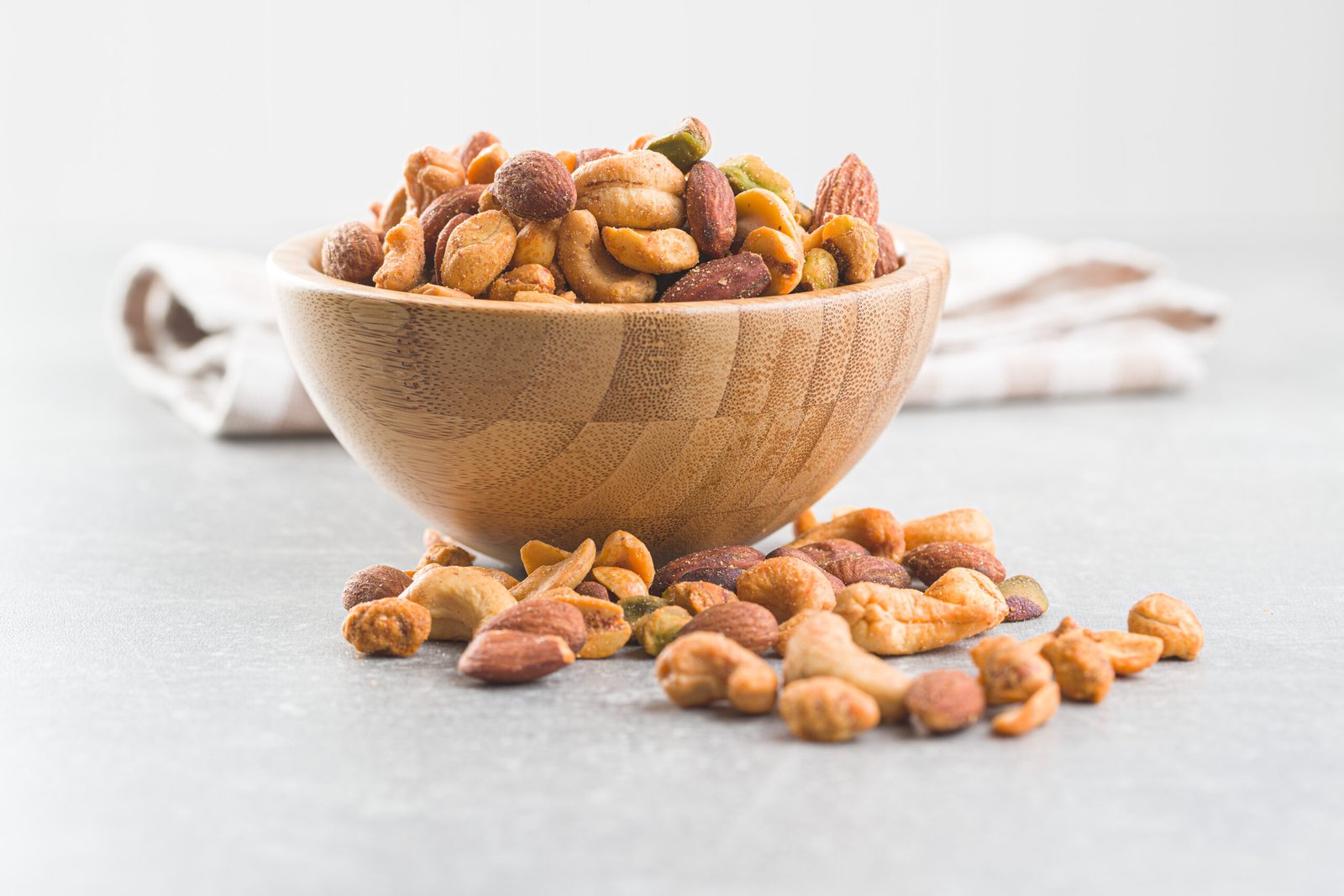 A bowl of flavored nuts standing on a grey background surface.
